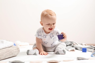 Sticker - Little boy in cute clothes sitting on floor against light background. Baby accessories