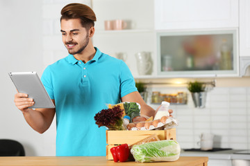 Canvas Print - Young man with tablet PC and products in kitchen. Food delivery service