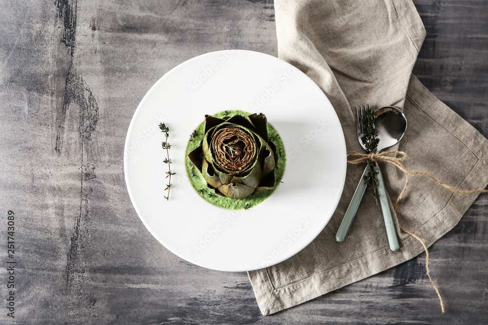 Plate with tasty cream soup and artichoke on table