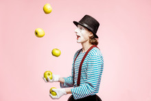 Pantomime With White Facial Makeup Juggling With Apples On The Pink Background In The Studio