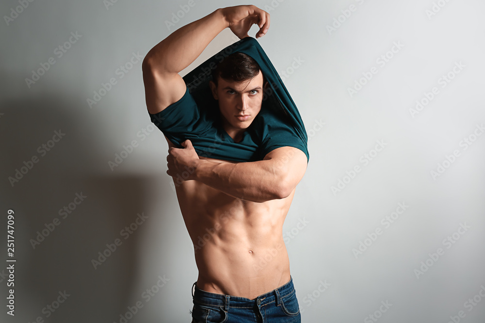 Muscular bodybuilder taking of his t-shirt on light background