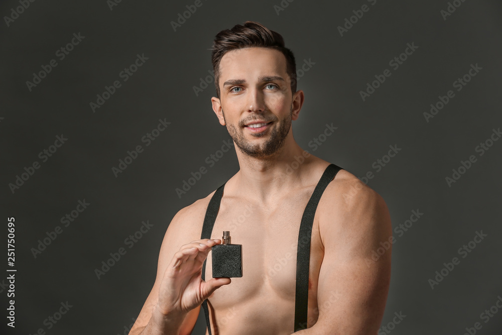 Handsome man with bottle of perfume on dark background