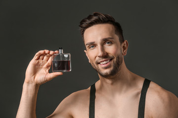 Wall Mural - Handsome man with bottle of perfume on dark background