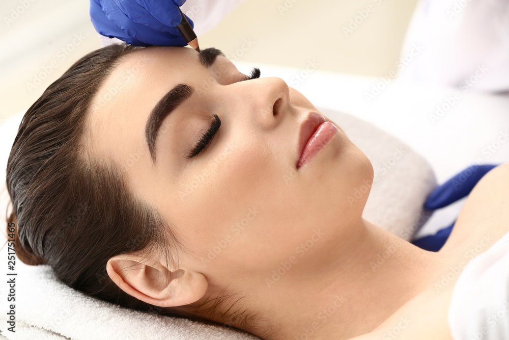 Young woman undergoing eyebrow correction procedure in beauty salon