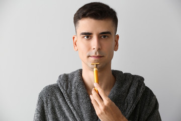 Poster - Man with facial massage tool on light background