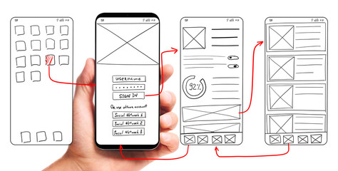 ui development. male hand holding smartphone with wireframed user interface screen prototypes of a m
