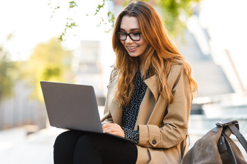 Canvas Print - Photo of joyous woman working on laptop while sitting on bench in city street