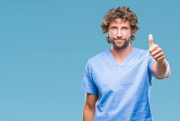 Wall Mural - Handsome hispanic surgeon doctor man over isolated background doing happy thumbs up gesture with hand. Approving expression looking at the camera with showing success.