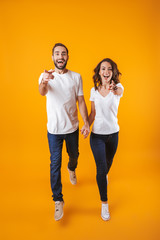 Wall Mural - Full length photo of cheerful couple holding hands while walking, isolated over yellow background
