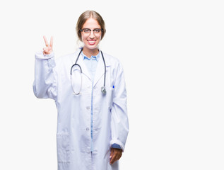 Sticker - Beautiful young blonde doctor woman wearing medical uniform over isolated background showing and pointing up with fingers number two while smiling confident and happy.