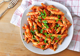 Wall Mural - Delicious pasta dish with fresh basil on a wooden table. Top view scene, healthy eating or healthy lifestyle. Penne napoli or pasta arrabiata, closeup shot.