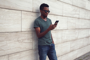 Canvas Print - african man with smartphone on city street, gray brick wall background