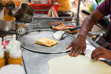 Cooking traditional Thai fried roti banana pancakes close up, asian street food preparation in Thailand, man chef hands frying pancakes on griddle in Bangkok, sweet fruit banana roti making on hot pan