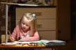© AliaksandrBS - Child preschooler learns to draw and write in notebooks at home in the evening under the light from a desk lamp.