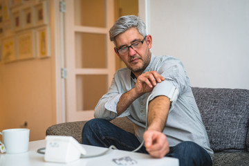 middle aged man measuring blood pressure at his apartment