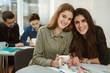 © Nestor - Crop of smiling happy beautiful girls looking at camera. Pupils drinking tea during lessons and feeling comfortable at classes. On background boys doing exercises and writing it down in copybooks.