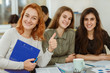 © Nestor - Crop of three beautiful happy girls sitting near one table nd doing common project. Young happy students smiling and showing like. Pupils enjoying their classes in school and relaxing during break.
