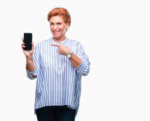 Sticker - Atrractive senior caucasian redhead woman showing smartphone screen over isolated background very happy pointing with hand and finger