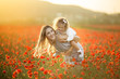 Beautiful child girl with young mother are having fun in field of poppy flowers over sunset lights