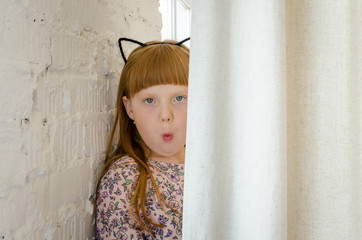 Surprised girl looking out from behind the curtains. A little girl with different emotions on her face