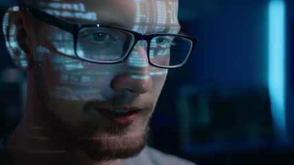 Wall Mural - Portrait of Software Developer / Hacker wearing Glasses Working on Computer, Projected Code Numbers and Characters Reflect on His Face. Dark Room Full of Technology. Zoom in Shot