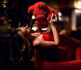 Beautiful young woman sitting in restaurant  celebrating birthday with cake and red bear of roses present gift