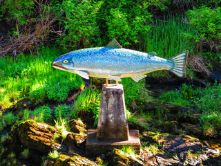 Silver mosiac salmon statue in Ketchikan set amongst greenery.