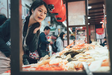 Vintage Picture Of Young Asian Girl Photographer Picking Many Seafood Sold In Kuromon Market In Osaka Japan. Chinese Woman Traveler Picking Choosing In Vendor In Black Door Ichiba Osaka Japan.