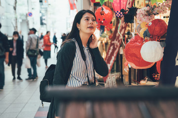 asian girl looking shopping in street vendor in kuromon ichiba in osaka japan. young chinese woman buying in japanese local traditional market in a toy lantern stand. travel photographer visiting.