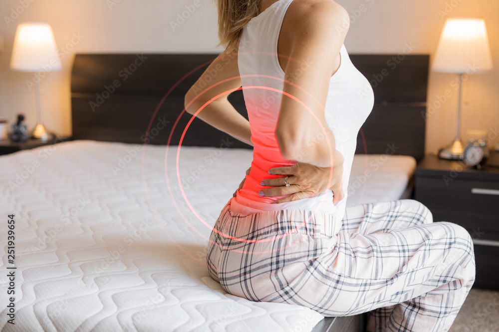Woman suffering from back pain because of uncomfortable mattress - obrazy, fototapety, plakaty 