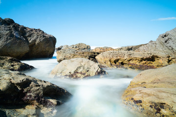 Poster - Waves smoothed by long exposure washing in around rocky foreshore at base of Mount Maunganui, Tauranga