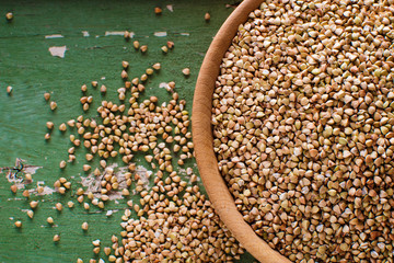 Wall Mural - Buckwheat in a wooden bowl on an old green wooden table, top view