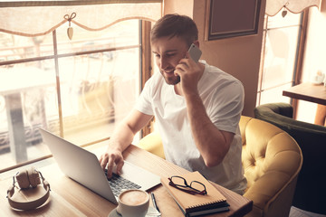 Canvas Print - Young freelancer talking on mobile phone while working on laptop in cafe