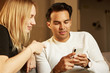 © KleverLevel - Beautiful young couple in casual clothes is using smartphones, looking at camera and smiling.