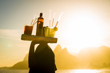 Scenic Sunset View Of Two Brothers Mountain With An Unrecognizable Silhouette Of A Beach Vendor Carrying Caipirinha Cocktails Passing In Silhouette At Arpoador In Rio De Janeiro, Brazil