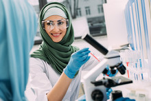 Smiling Female Muslim Scientist In Goggles And Hijab During Experiment In Chemical Laboratory