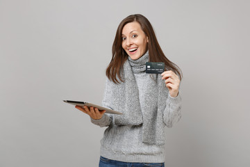 Wall Mural - Excited young woman in gray sweater, scarf using tablet pc computer and holding credit bank card isolated on grey wall background. Healthy lifestyle, online treatment consulting, cold season concept.