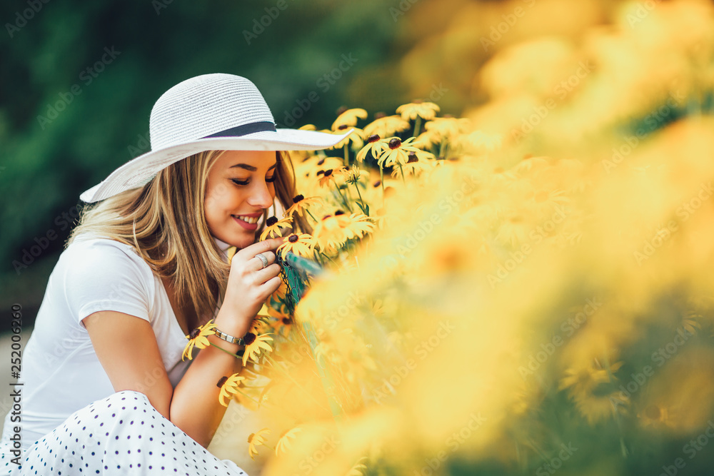 Beautiful young woman smelling yellow flower in the park. - obrazy, fototapety, plakaty 