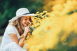© Mediteraneo - Beautiful young woman smelling yellow flower in the park.