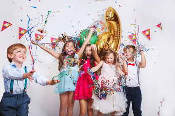 Group of beautiful kids throwing colorful confetti and looking happy on birthday party