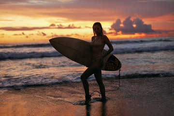 Wall Mural - Surfer girl with surf board on sunset beach on summer vacation