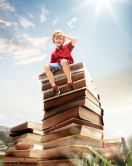 Little boy sitting on the tower made of big books. Childhood dreams, reading and education concept. Wondering world. abstract collage