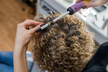 Wall Mural - master doing curls, curl the hair with Curling iron, girl with blonde hair, close-up