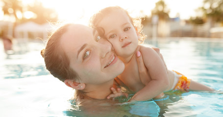 Mom and little daughter are played in the open swimming pool. Family with one child on vacation in warm countries. Positive people on vacation.