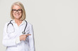 © fizkes - Smiling doctor with stethoscope pointing at copyspace isolated on background