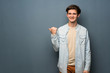 © luismolinero - Teenager man with jean jacket over grey wall pointing to the side to present a product