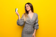 © luismolinero - Young woman with glasses over yellow wall holding a credit card and thinking