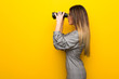 © luismolinero - Young woman with glasses over yellow wall and looking in the distance with binoculars