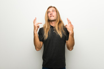 Wall Mural - Blond man with long hair over white wall with fingers crossing and wishing the best