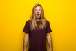 Blond man with long hair over yellow wall with surprise and shocked facial expression